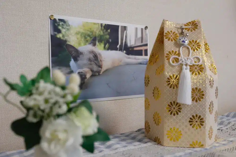 a pet memorial of an urn covered in a golden floral design next to a photo of a cat and some flowers